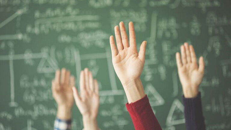 Hoch gehaltende Hände vor einer Schultafel