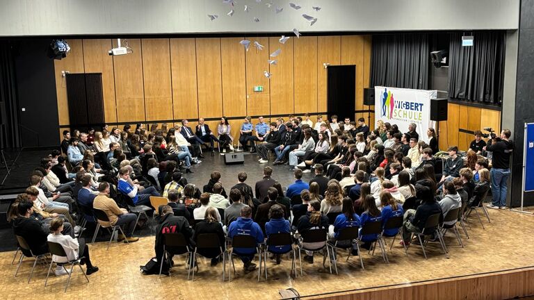 Schüler und Schülerinnen sitzen in einem Stuhlkreis in der Aula einer Schule