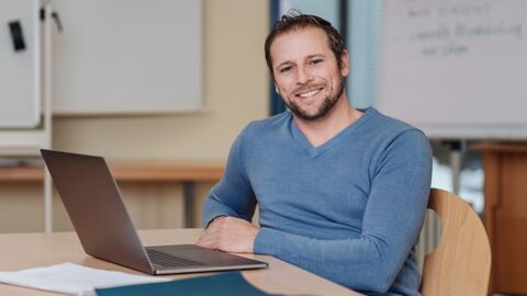 Lehrer sitzt vor einem Laptop.