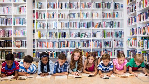 Schülerinnen und Schüler lesen mit ihrer Lehrerin in der Schulbibliothek. Schülerinnen und Schüler lesen mit ihrer Lehrerin in der Schulbibliothek.