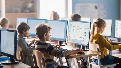 Grundschüler sitzen im Computerraum und lernen mit PCs. 