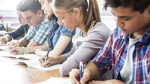Schülerinnen und Schüler schreiben im Unterricht in ihre Hefte. Schülerinnen und Schüler schreiben im Unterricht in ihre Hefte.
