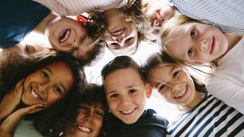 Schülerinnen und Schüler stehen in einem Kreis zusammen und schauen in die Kamera. 