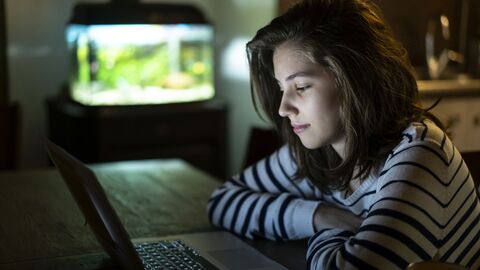 Mädchen sitzt nachts vor dem Laptop.