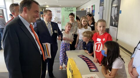 Kultusminister Lorz steht vor einem Stand von Schülerinnen und Schülern und lächelt sie an.