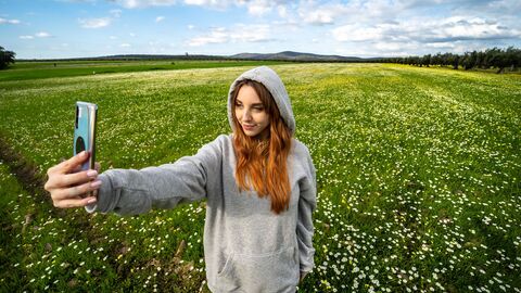 Mädchen macht auf einer Wiese ein Selfie. 