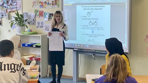 Förderung für ukrainische Kinder und Jugendliche in Hessens Schulen Eine Lehrerin steht am Whiteboard vor der Klasse und hält einen Zettel in der Hand. Die Schülerinnen und Schüler schauen aufmerksam zu.