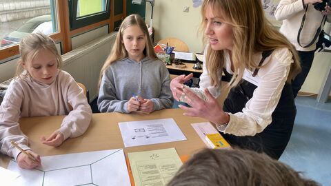 Förderung für ukrainische Kinder und Jugendliche in Hessens Schulen Die Lehrerin steht bei einer Gruppe Schülerinnen am Tisch und erklärt eine Aufgabe. Vor den Schülerinnen liegt ein Blatt Papier und eine Aufgabenstellung.
