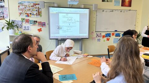Kultusminister Lorz am Gruppentisch mit Schülerinnen, die in Aufgaben vertieft sind. Im Hintergrund ein Whiteboard mit einer Aufgabenstellung.
