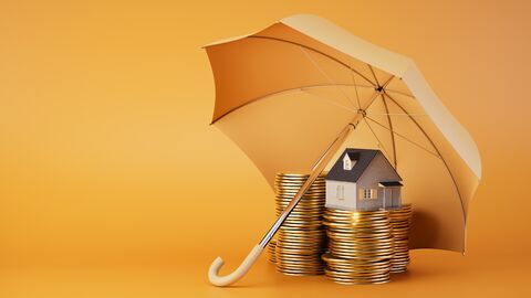 Ein Regenschirm schützt einen Haufen Münzen und ein Miniaturhaus.