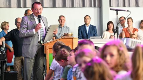 Kultusminister Lorz mit Mikrofon in der Hand an einem Podium, im Vordergrund viele Kinder
