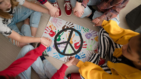 Jugendliche sitzen im Kreis um ein Friedenszeichen herum. Jugendliche sitzen im Kreis um ein Friedenszeichen herum.