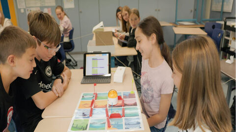 Schüler sitzen um Tablet und Aufgabe