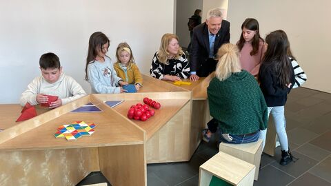 Kultusstaatssekretär Lösel gemeinsam mit Schülerinnen und Schülern sowie Lehrkräften an einem Tisch mit Matherätseln.