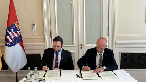 Demetrios Nicolaides und Armin Schwarz sitzen an Tisch und unterschreiben eine Vereinbarung