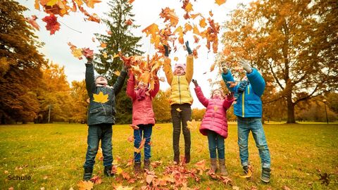Kinder werfen bunte Blätter in die Luft. 