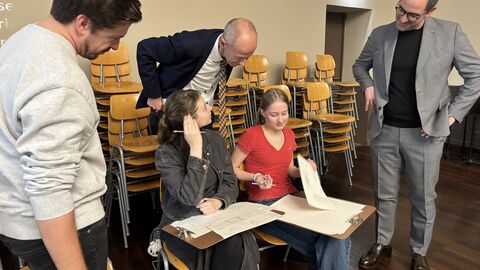 Bildungsminister Schwarz schaut über die Schulter von zwei Schülerinnen, wie sie gerade am Tisch sitzen und etwas schreiben.