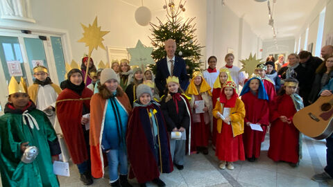 Eine größere Gruppe von Sternsingern stehen gemeinsam mit Minister Armin Schwarz in einem Gebäude vor einem Weihnachtsbaum