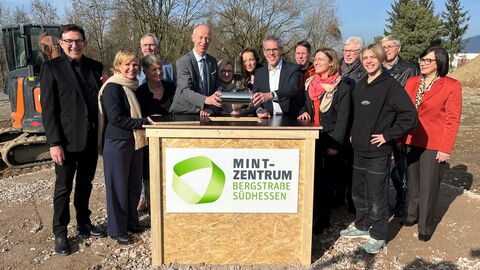 Grundsteinlegung MINT-Zentrum Bergstraße Südhessen Mehrere Personen stehen auf einer Baustelle um einen provisorischen Tisch mit der Aufschrift "MINT-Zentrum Bergstraße Südhessen" herum.