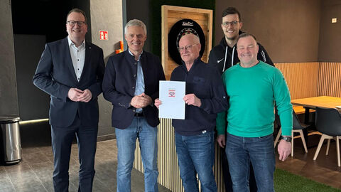 Fünf Männer stehen nebeneinander. Der mittlere hält einen Förderbescheid hoch.