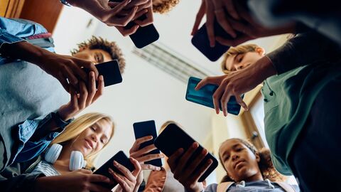 Jugendliche stehen in einem Kreis und schauen auf ihr Handy Jugendliche stehen in einem Kreis und schauen auf ihr Handy