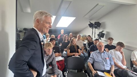 Eine Schulklasse sitzt verteilt auf Stühlen und schaut nach vorne.