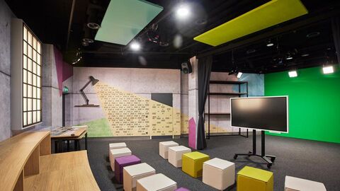 Ein modern ausgestatteter Medienraum mit Bestuhlung, einem interaktiven Bildschirm und einer Greenscreen-Wand. Der Raum verfügt über eine Tribüne und ist für Video- und Medienproduktionen konzipiert.