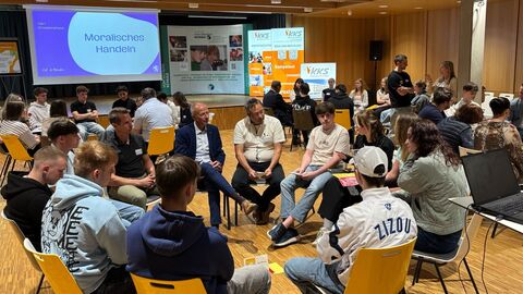 Bildungsminister Schwarz sitzt mit Schülerinnen und Schülern in einem Stuhlkreis