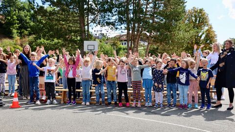 Starke Kinder Eine große Gruppe von Schülerinnen und Schülern steht eng beieinander im Freien. Sie singen gemeinsam und haben dabei die Arme nach oben gestreckt.