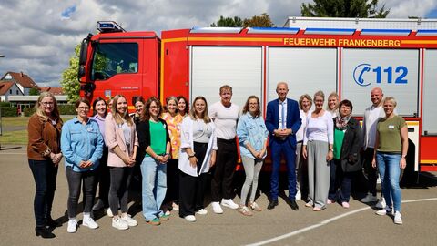Engagement für Werte: Lehrkräfte und Kultusminister Seite an Seite Kultusminister Armin Schwarz steht gemeinsam mit Lehrerinnen und Lehrern vor einem roten Löschgruppenfahrzeug der Feuerwehr Frankenberg auf dem Schulhof.