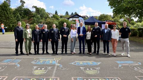 Gemeinsam für Werte auf dem Schulhof Auf dem Schulhof stehen Mitglieder der Hessischen Jugendfeuerwehr in blauen Uniformen zusammen mit Lehrkräften, der Schulleiterin und Kultusminister Armin Schwarz. Auf dem Boden sind bunte Kreidezeichnungen zu sehen.