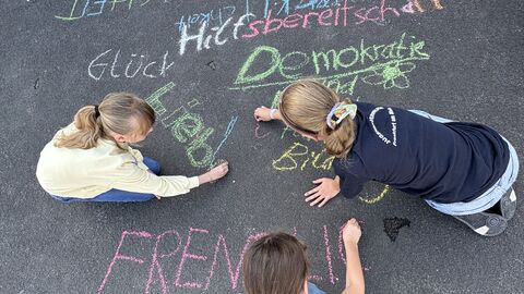 Schülerinnen und Schüler ergänzen Kreideworte Schülerinnen schreiben ihre Werte mit bunter Kreide auf den Schulhof