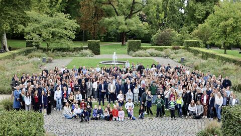 Weitwinkelaufnahme einer großen Gruppe von über hundert Personen in einem Park, alle stehen zusammen und blicken in die Kamera.