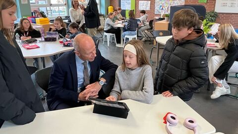 Ein Mann sitzt an einem Tisch mit einer Schülerin. Beide schauen auf ein Tablet während sie spricht.