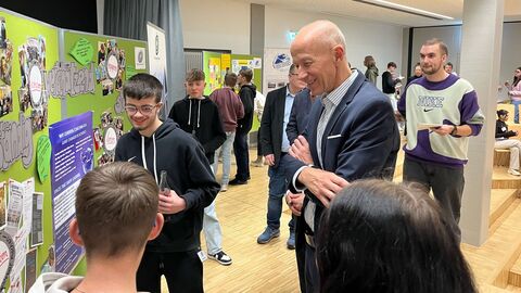 Armin Schwarz steht gemeinsam mit Schülern vor einer großen Kollage, auf der u.a. das Wort "wertschätzend" zu sehen ist.