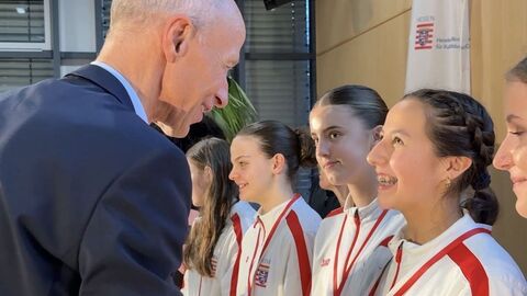 Bildungsminister Armin Schwarz steht vor einer Schülerin in Sportkleidung, die glücklich lächelt.