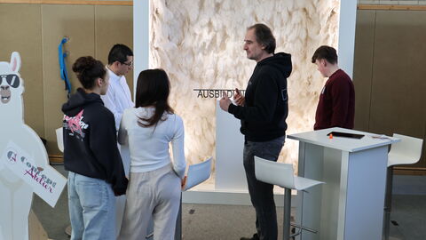 Eine Gruppe Jugendlicher hört auf einer Messe einem Standbetreiber zu
