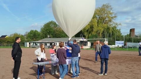 Schülerinnen und Schüler stehen auf einem Platz und halten einen großen Luftballon hoch.