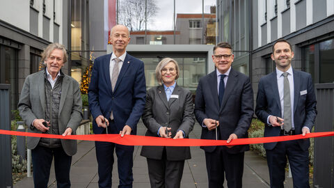 v.l.n.r.: Eigentümer Andrzej Lyson, Bildungsminister Armin Schwarz, Evelin Spyra, Leiterin des Staatlichen Schulamts, Ministerpräsident Boris Rhein, Carsten Mergenthaler von der Lehrkräfteakademie) Fünf Personen stehen vor einem Gebäude mit jeweils einer Schere in der Hand. Vor ihnen ein rotes Band welches sie gemeinsam durchschneiden.